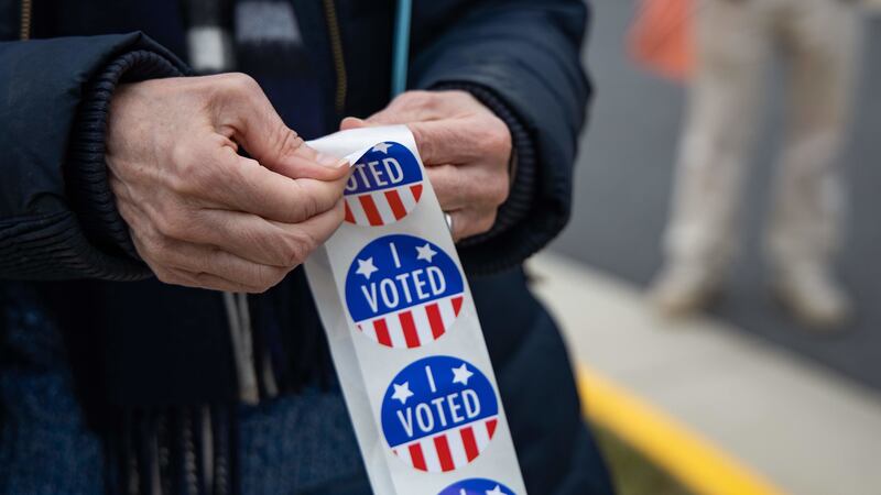 A Fairfax Democrats member peels a sticker for a voter at Langley High School.