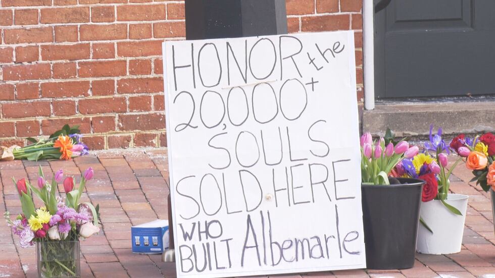 A sign and flowers on the ground at the site of a former Charlottesville slave auction block.